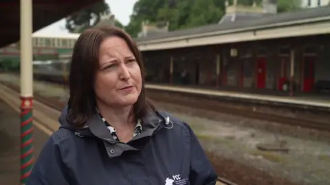 BBC A picture of Alison Hernandez standing at a train station. She is wearing a black coat and has brown hair.