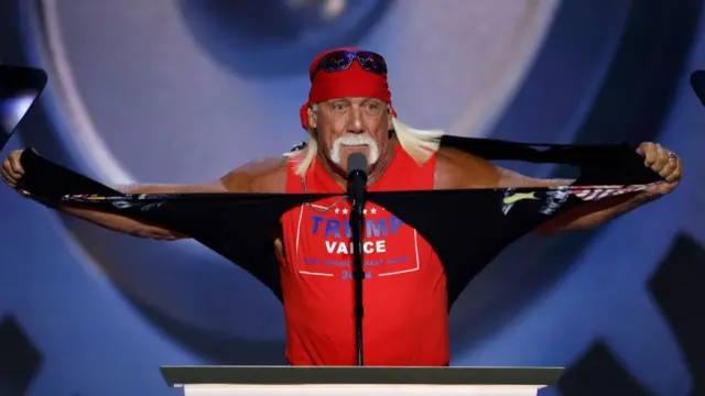 Hulk Hogan rips his shirt as he speaks on stage. He rips a black shirt to reveal a red Trump-Vance 2024 campaign shirt.