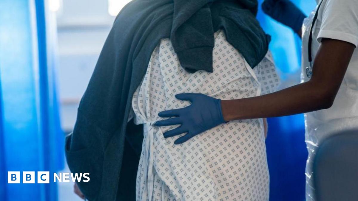 Image shows a patient being led by a member of staff on a NHS hospital ward at Ealing Hospital in London