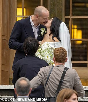 Meanwhile George wore a dark double breasted suit over a light open collared shirt with a flower, that matched his wife's bouquet, in his button hole