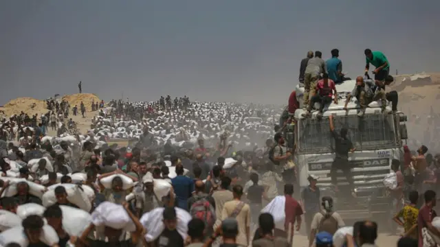 Internally displaced Palestinians carry bags of flour near a food distribution point in Zikim, northern Gaza Strip, 27 July 2025.