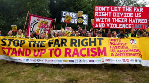 Simon Dedman/BBC A large banner being held up by a lot of people, it reads 'Stop the far right. Stand up to racism.