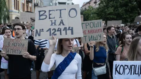 Getty Images Young Ukrainians in Kyiv hold placards, including a young woman with a white T-shirt and a blue sash