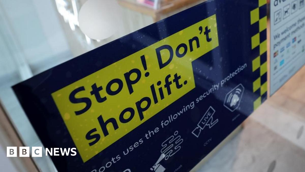 A group of young woman walk along a street past a sign that reads "Stop! Don't Shoplift".