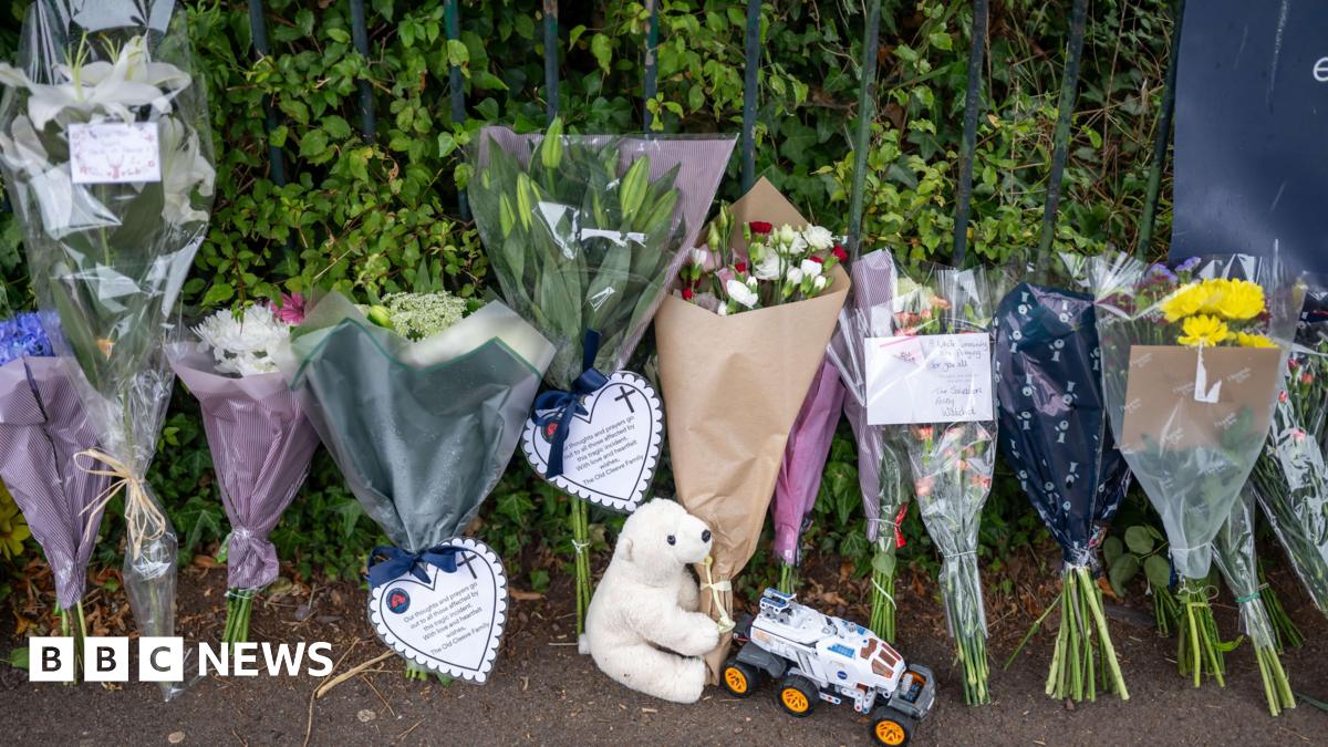 Several bouquets of flowers laid in tribute to a boy who died. Many of them include notes and cards. There is also a teddy and a toy car on the ground.