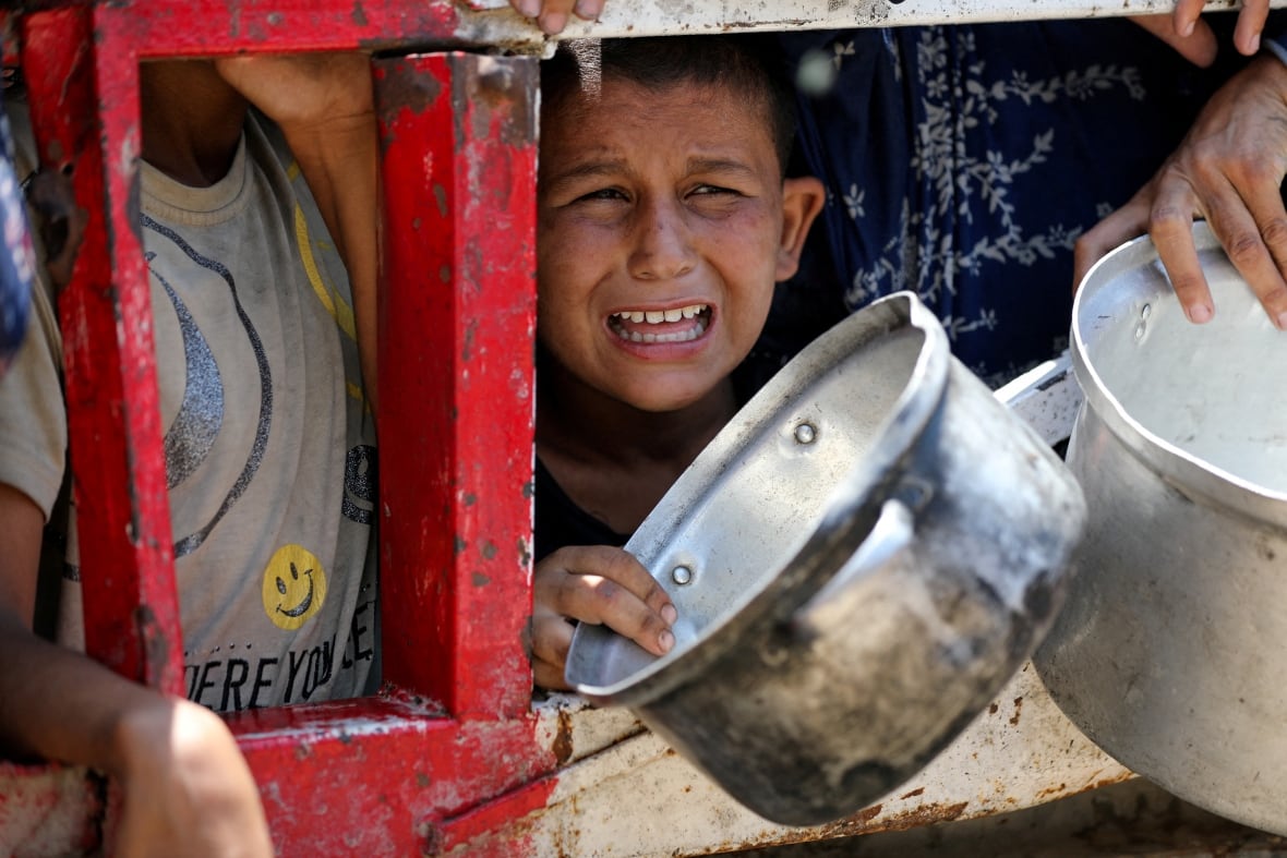 A child cries as he extends his arm with an empty pot in hand.
