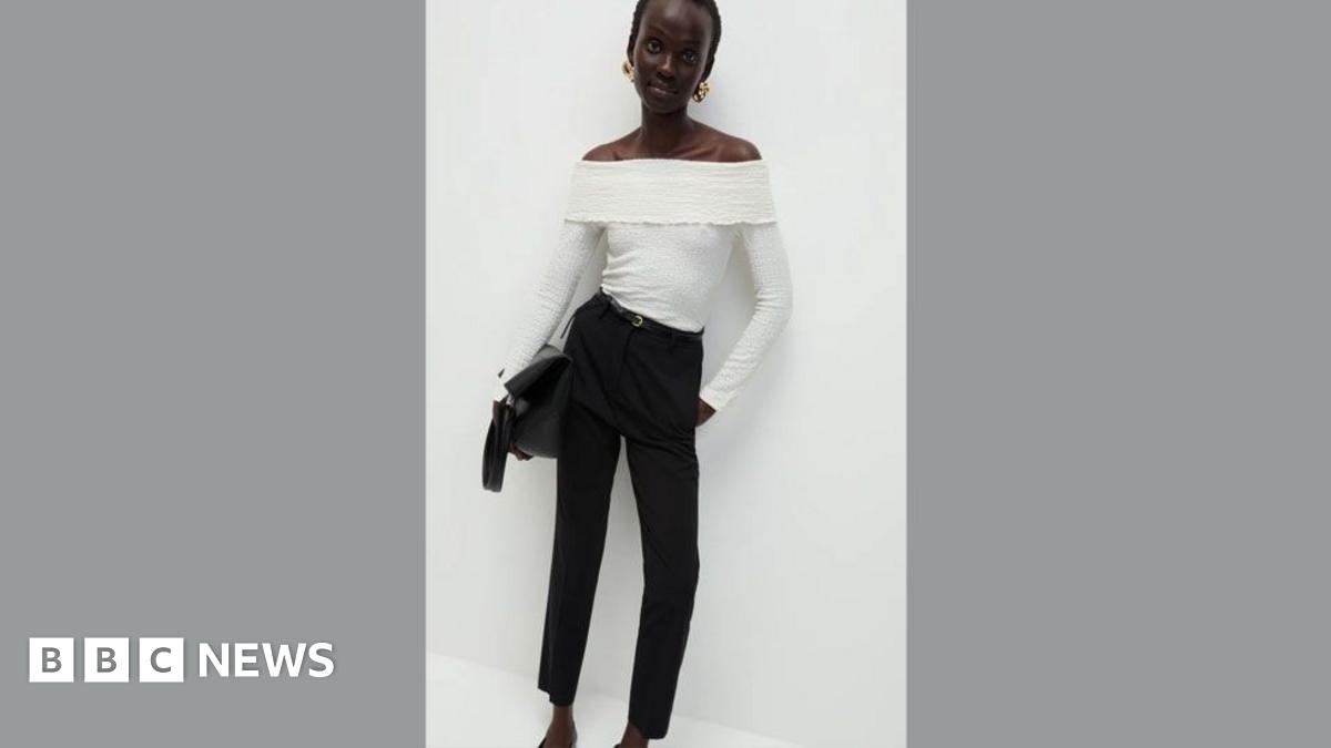 M&S model poses in white top and black trousers and leans against a white wall