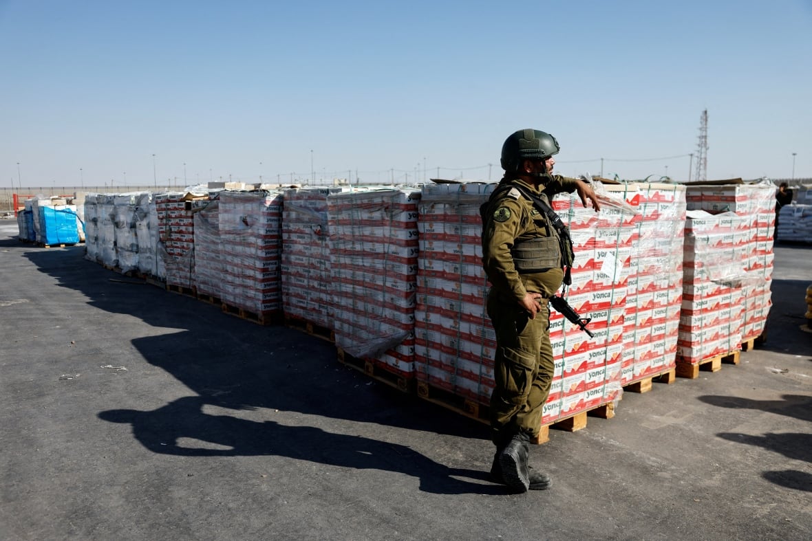 A soldier leans on pallets of humanitarian aid. 