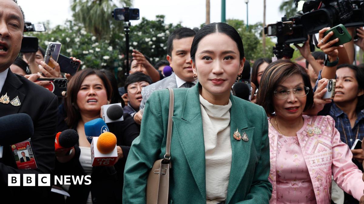 Thai Prime Minister Paetongtarn Shinawatra is surrounded by journalists after a cabinet meeting at Government House in Bangkok, Thailand, 01 July 2025. She wears a green suit, and the journalists are holding microphones, cameras and phones toward her.