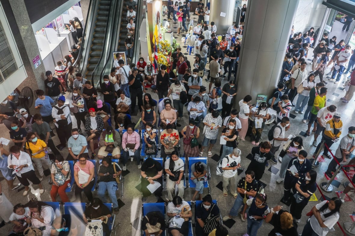 An overhead view shows dozens of people seated and standing in an indoor area.