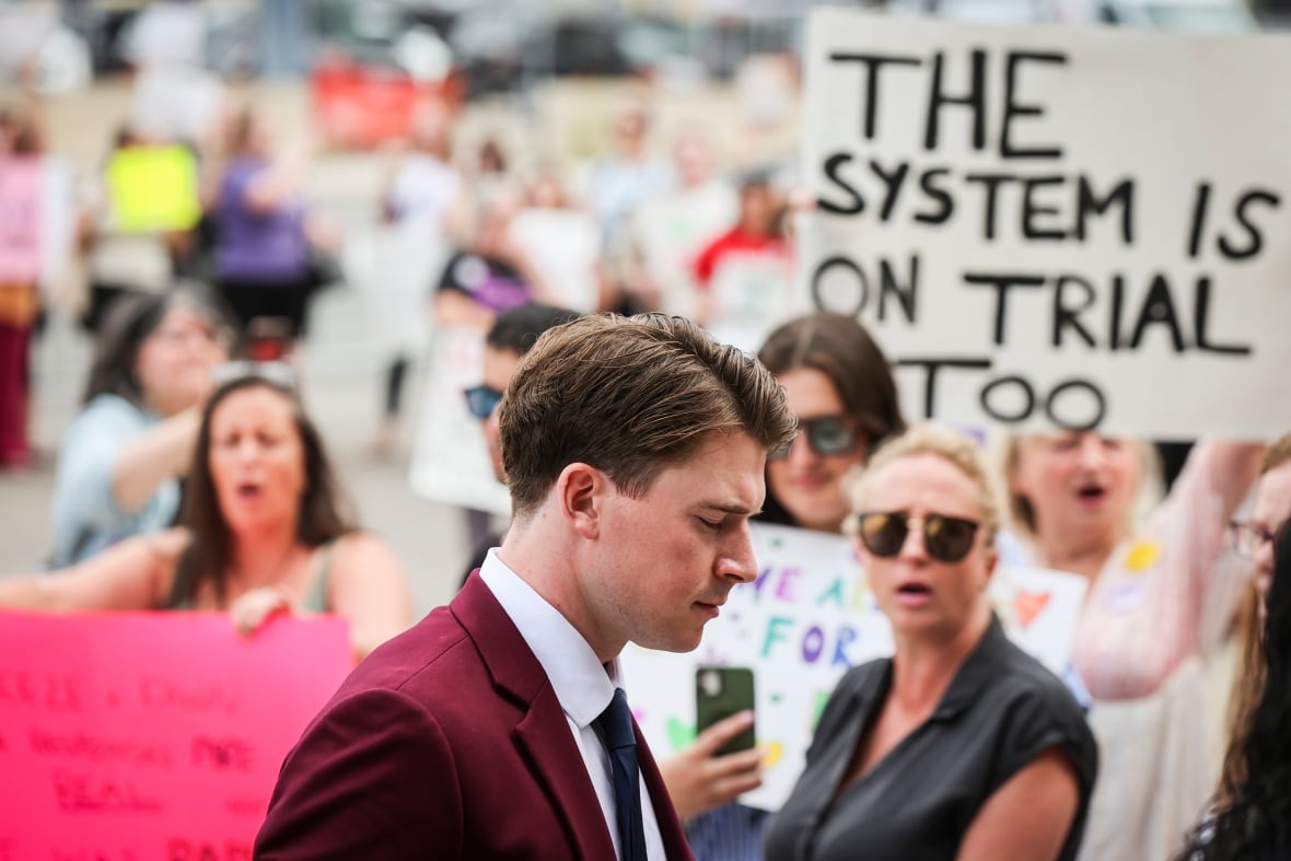 A man in a red suit walks by a group of people holding signs on a sidewalk.
