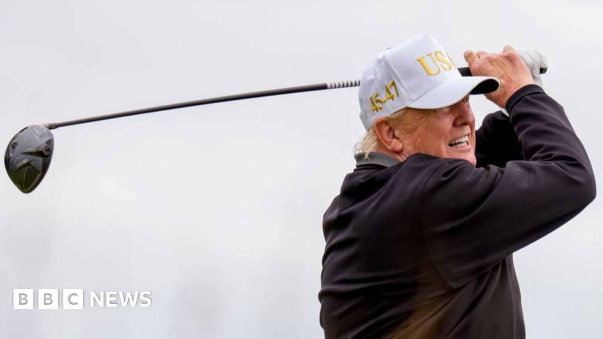 President Donald Trump tees off at a new 18-hole course at Trump International Golf Links in Balmedie, near Aberdeen. He is wearing a white USA baseball cap and is at the end of his golf swing with the driver held aloft behind his head
