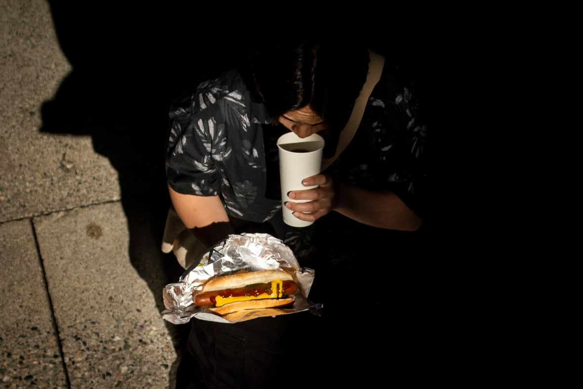 A person holds a  hot dog and sips adrink