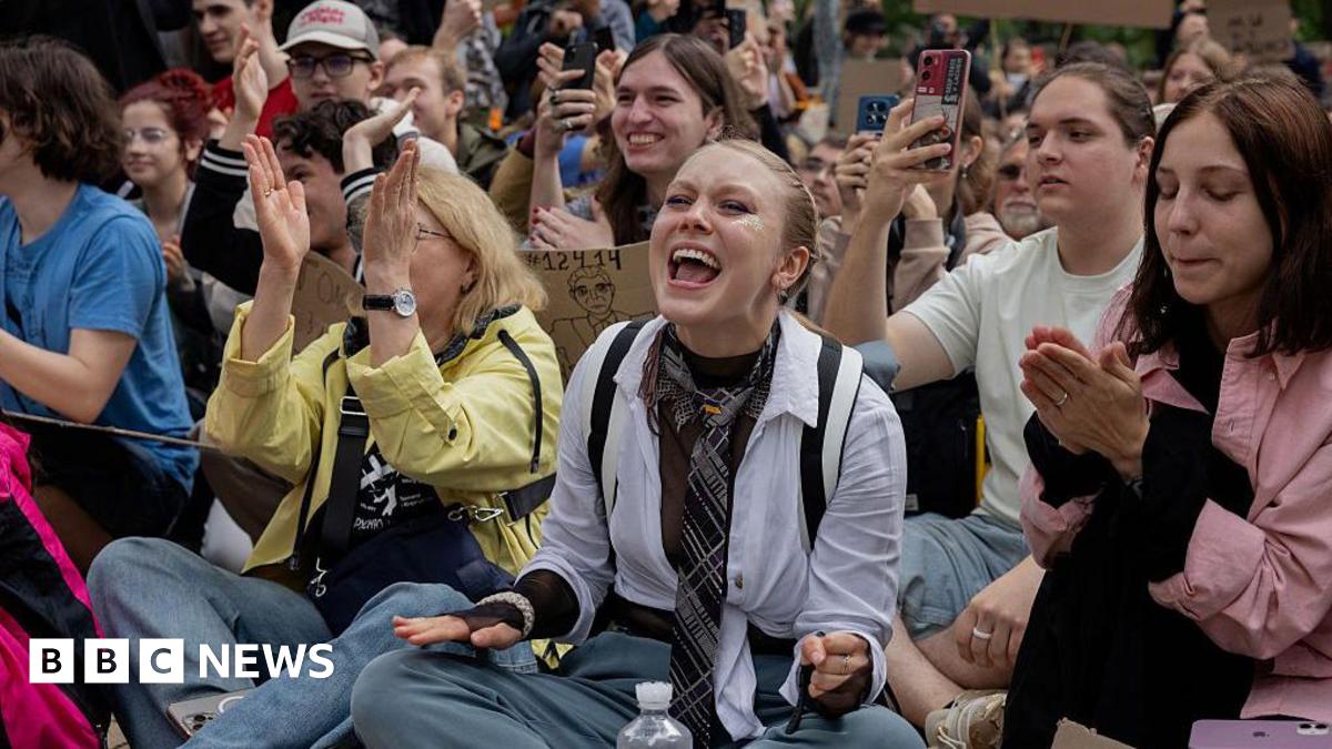 Young Ukrainians sit outside parliament clapping and holding placards