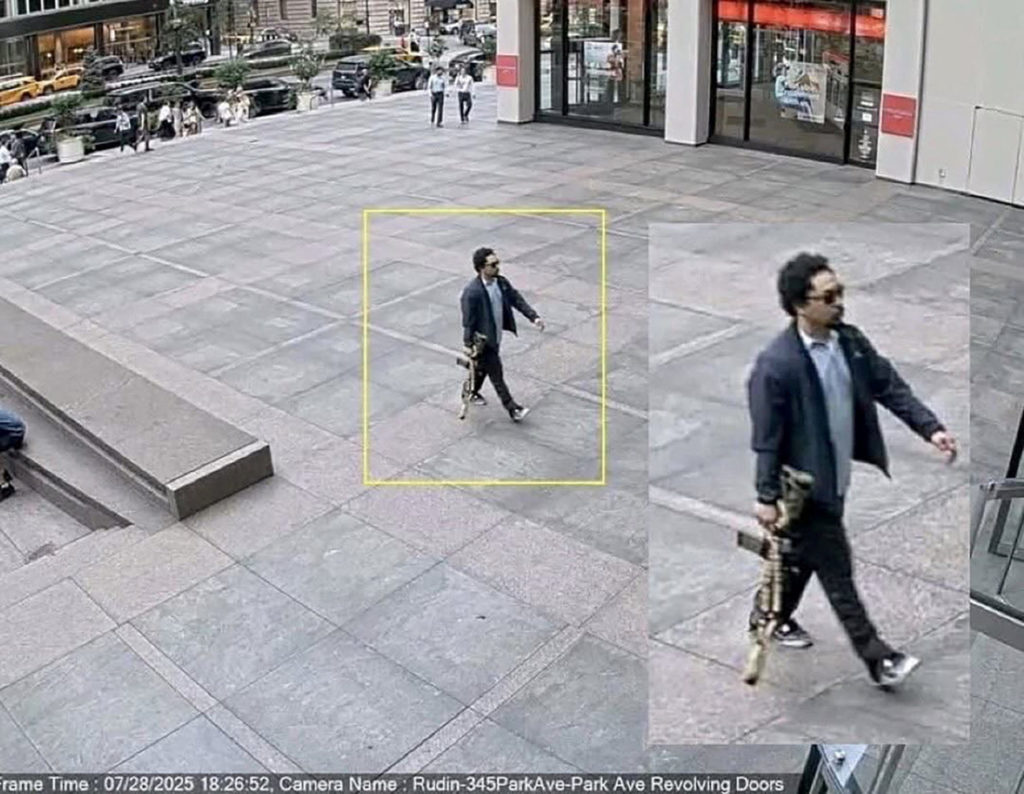 A man holding a rifle walks into an office building shortly before a shooting that killed several people in Manhattan