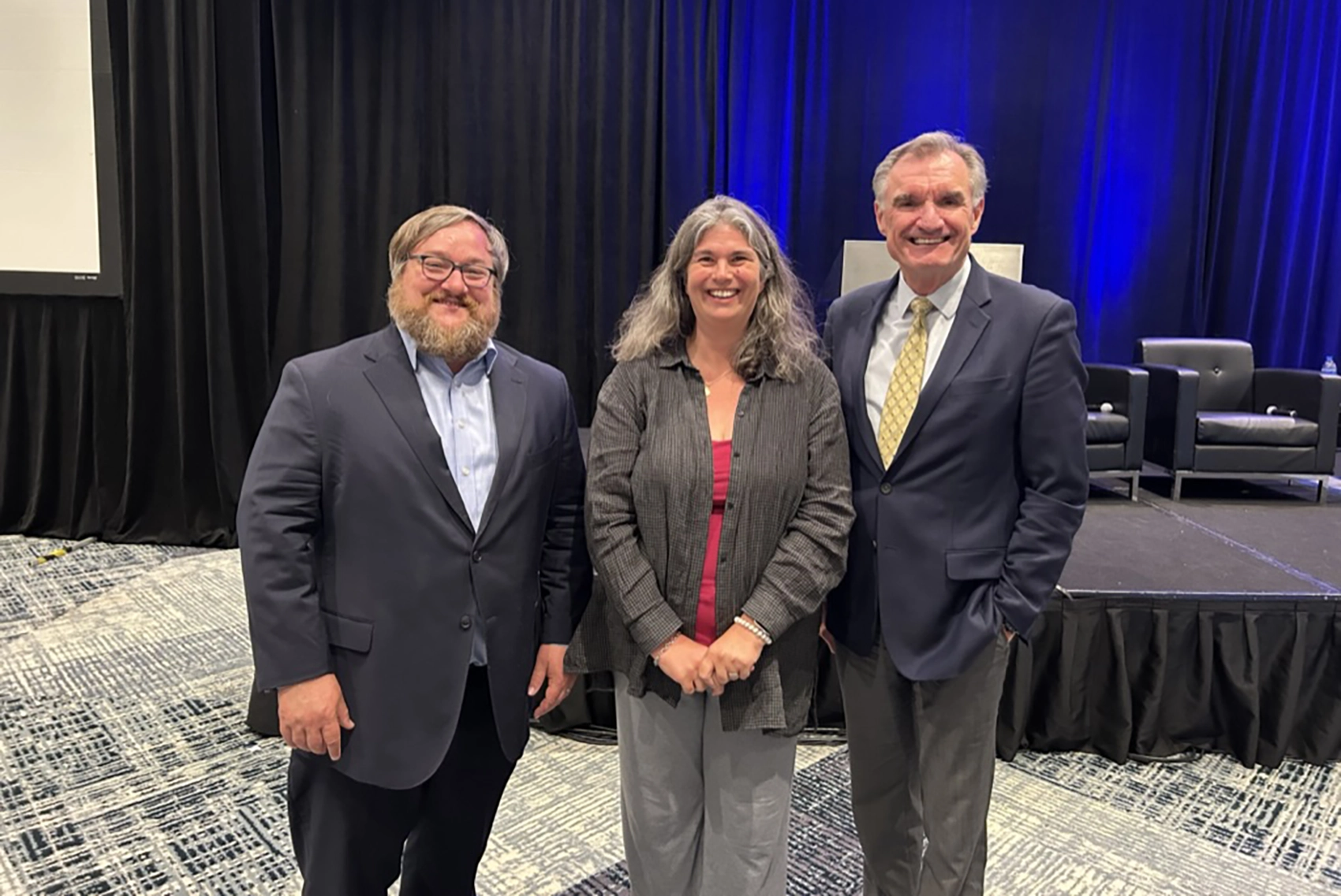Three people pose in front of a stage.