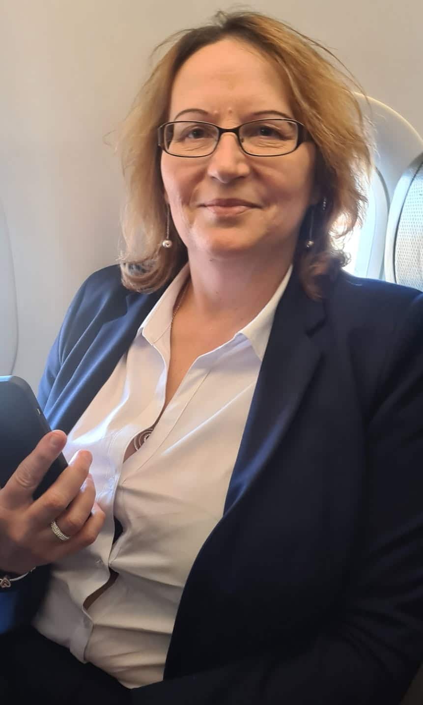 A woman sits in the window seat of an aeroplane holding up a smartphone in her right hand.