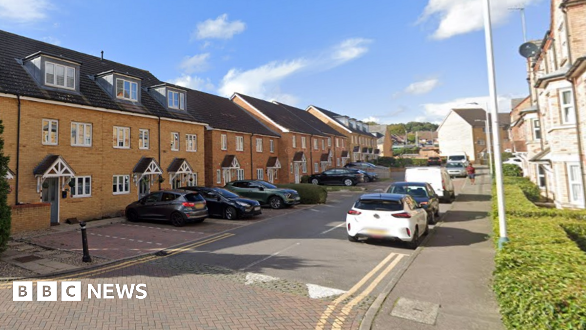 A row of brick houses with and parked cars on both sides of a narrow street.