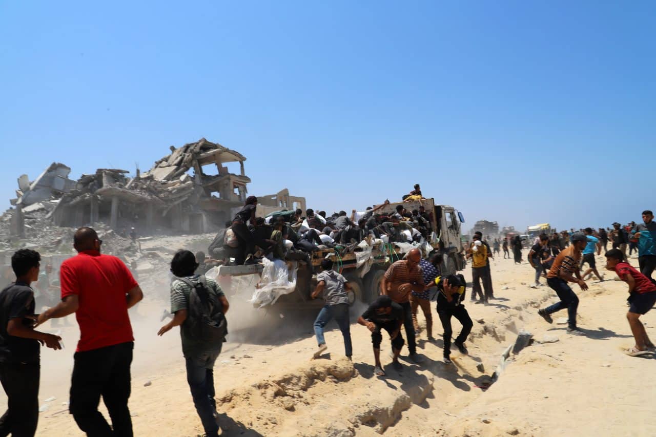 People make their way along al-Rashid street in Western Jabalia toward trucks carrying humanitarian aid after entering the northern Gaza Strip through the Israeli-controlled Zikim border crossing, July 22, 2025. (Photo: Abdullah Abu Al-Khair/APA Images)