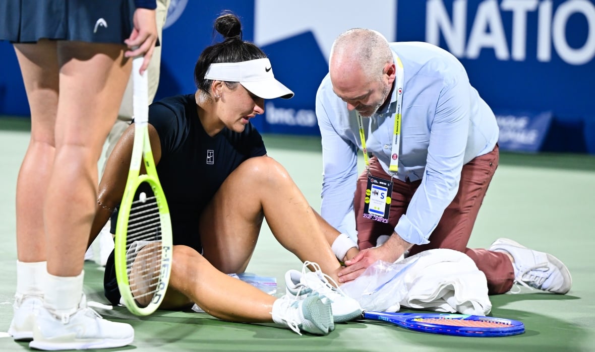 A women's tennis player lays on the ground to be examined by medical staff.