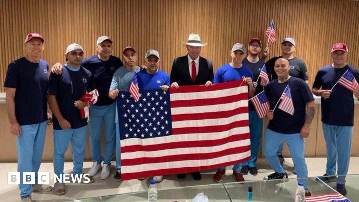 Several men in jeans carrying a large American flag pose for photo