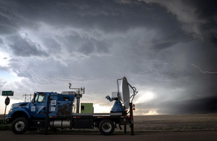 Dark storm clouds and lightning with a large truck carrying a satellite and other equipment in its flatbed.