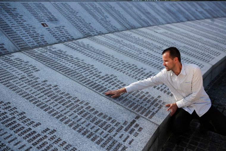 Nedzad Avdic touches the engraved names on a large stone memorial