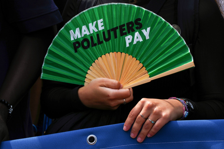 An activist holds a fan that reads "make polluters pay"