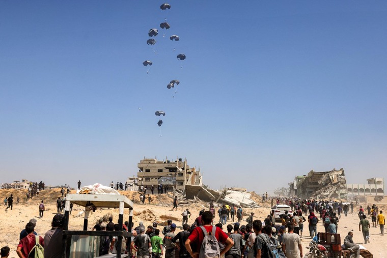 People gather as a C-130 Hercules military transport aircraft drops humanitarian aid on the northern Gaza Strip on July 27, 2025. 