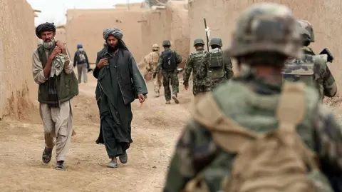 Getty Images Afghan men walk past a patrol conducted by British soldiers of the 1st batallion of the Royal Welsh, French soldiers of the 21st RIMA and Afghan soldiers in a street of the city of Showal in Nad-e-Ali district, Southern Afghanistan, in Helmand province on February 25, 2010. 