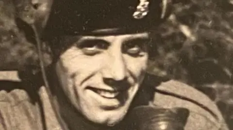 Family handout A black and white picture of a man in military uniform. He is smiling at the camera and has a badge on his beret