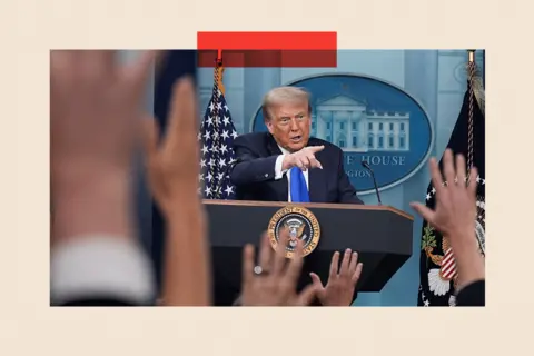 Getty Images Trump points at an audience, standing behind a lectern, while people raise their hands to ask questions