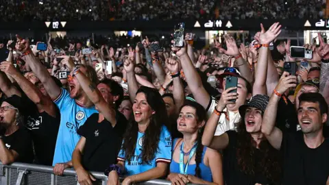 Getty Images Oasis fans at the Principality Stadium. A large number of people can be seen looking towards the stage. Many have their hands in the air and are recording the concert on their smartphones.