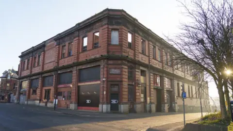 Getty Images An old Victorian red brick building viewed from the corner, with empty roads feeding off to left and right. The building appears derelict with some windows and doors boarded up.