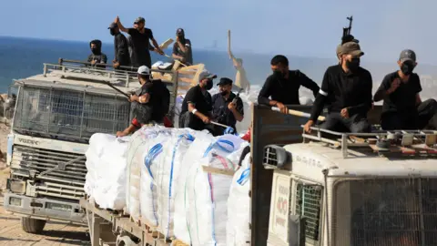 Reuters Armed members of a local Palestinian clan sit on top of a UN aid convoy to protect it, near Beit Lahia, in northern Gaza (25 June 2025)