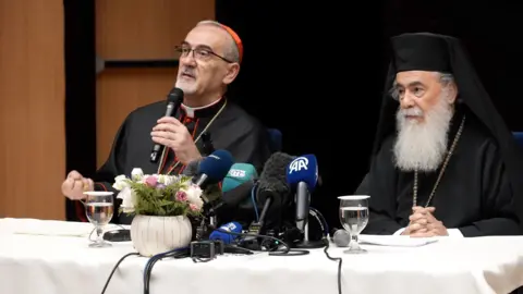 Jimmy Michael / BBC Speaking in front of microphones on top of a white table the Latin Patriarch Cardinal Pierbattista Pizzaballa and Greek Orthodox Patriarch Theophilos III address reporters in Jerusalem on 22 July 2025