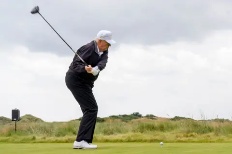 PA Media President Trump, a man in dark clothes, white shoes and cap teeing off on a golf course