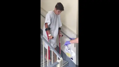 Family handout Ed Caudwell coming down the stairs at the hospital after his accident. He is  being assisted by staff and he is on crutches.