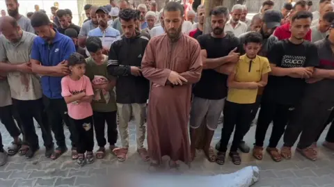 Men and boys pray beside the body of a child killed in an Israeli air strike that hit a water distribution point on 13 July 2025