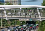 A sign on the Blumenauer Pedestrian Bridge reads “protect our rights, not ICE” in Portland, Ore., July 17, 2025 while Indivisible Oregon member Keir Karson waves an American flag.. These “Good Trouble” demonstrations in various areas around Portland were part of a nationwide effort to protest against the Trump Administration in the name of the late congressman John Lewis of Georgia. 