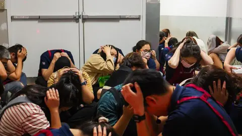 Getty Images Shoppers and supermarket employees crouch and cover their heads and ears in an underground shelter during an air raid evacuation rehearsal in Taipei