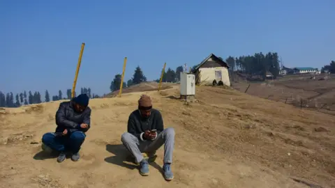 Getty Images People are resting in the dry meadows, which are usually covered in a thick blanket of snow during winters, at Gulmarg, a ski destination in the Baramulla district of Indian-administered Kashmir, on January 23, 2024
