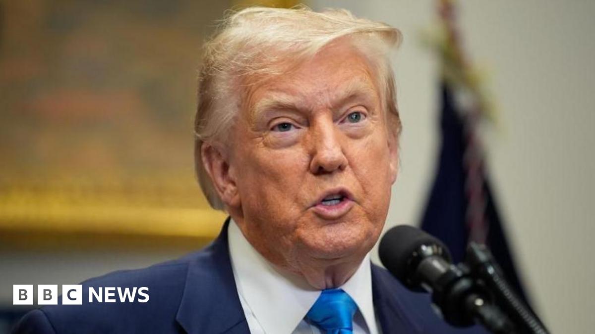 US President Donald Trump - wearing a dark blue jacket, white shirt and mid-blue tie - speaks in front of a microphone.