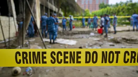 Getty Images A crime scene barrier tape cordons off the area as Bangladesh Air Force personnel inspect the crash site a day after a training jet crashed into a school in Dhaka