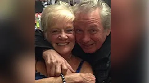 Police handout Sheila Jackson with blond hair smiles as Eric Greener with grey hair has his arm around her neck in front of a bar. Eric is also smiling.