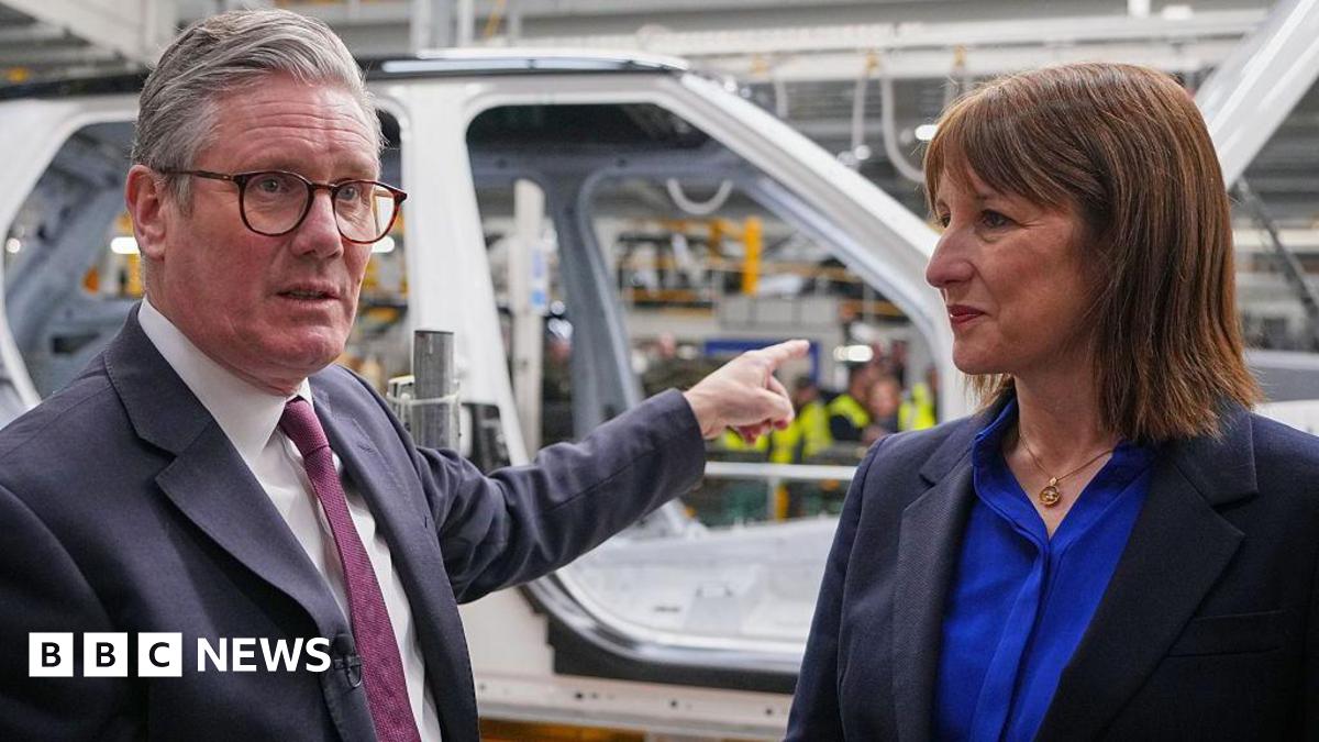 Prime Minister Keir Starmer stands to the left of Chancellor Rachel Reeves and gestures as at a car being built during a visit to a Jaguar Land Rover car factory in Birmingham.