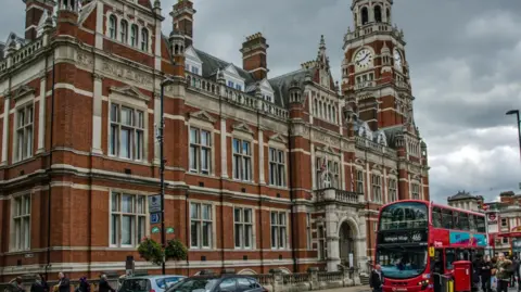 PA Media Croydon town hall, a red brick building with flags outside and a red bus at a stop.