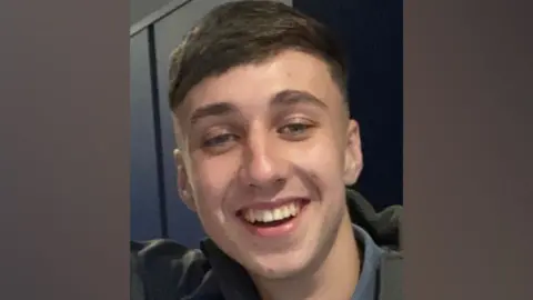 BBC A photograph of Jay Slater, in close-up. He is smiling at the camera