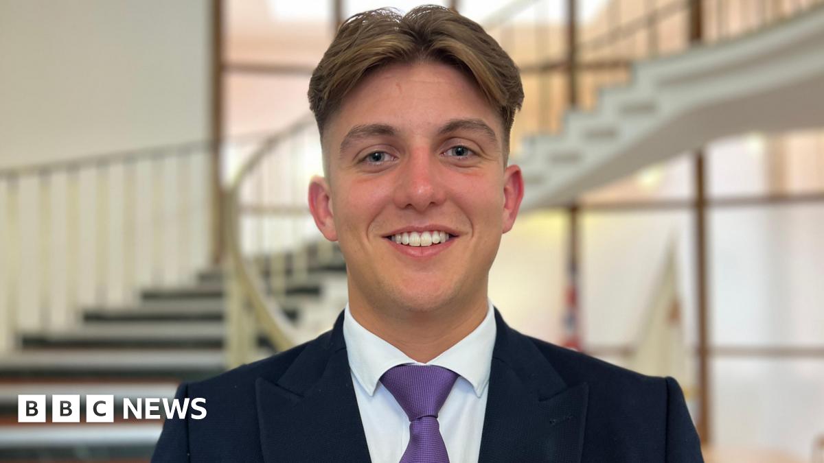 George Finch wears a purple tie and smiles at the camera.