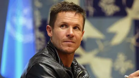 Getty Images Felix Baumgartner looks off to the side. He has blue eyes and short brown hair. He is wearing a leather jacket.